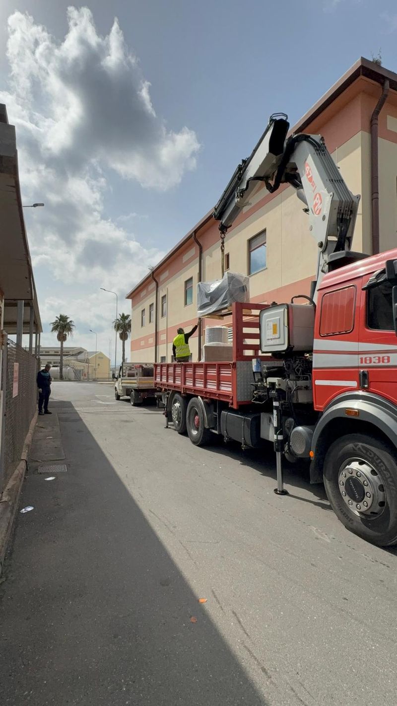 Camion con gru che scarica un macchinario davanti a un edificio, durante un cantiere