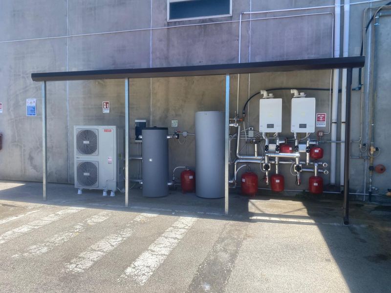 Centrale termica esterna con pompa di calore, accumuli e caldaie a muro sotto una tettoia