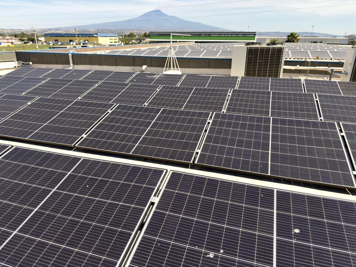 Impianto fotovoltaico industriale sul tetto di un capannone, con l'Etna sullo sfondo
